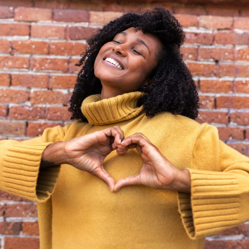 Happy, smiling young African American woman making heart shape with hands in front of chest. Happy, smiling young African American woman making heart shape with hands in front of chest. Love and romance concept.